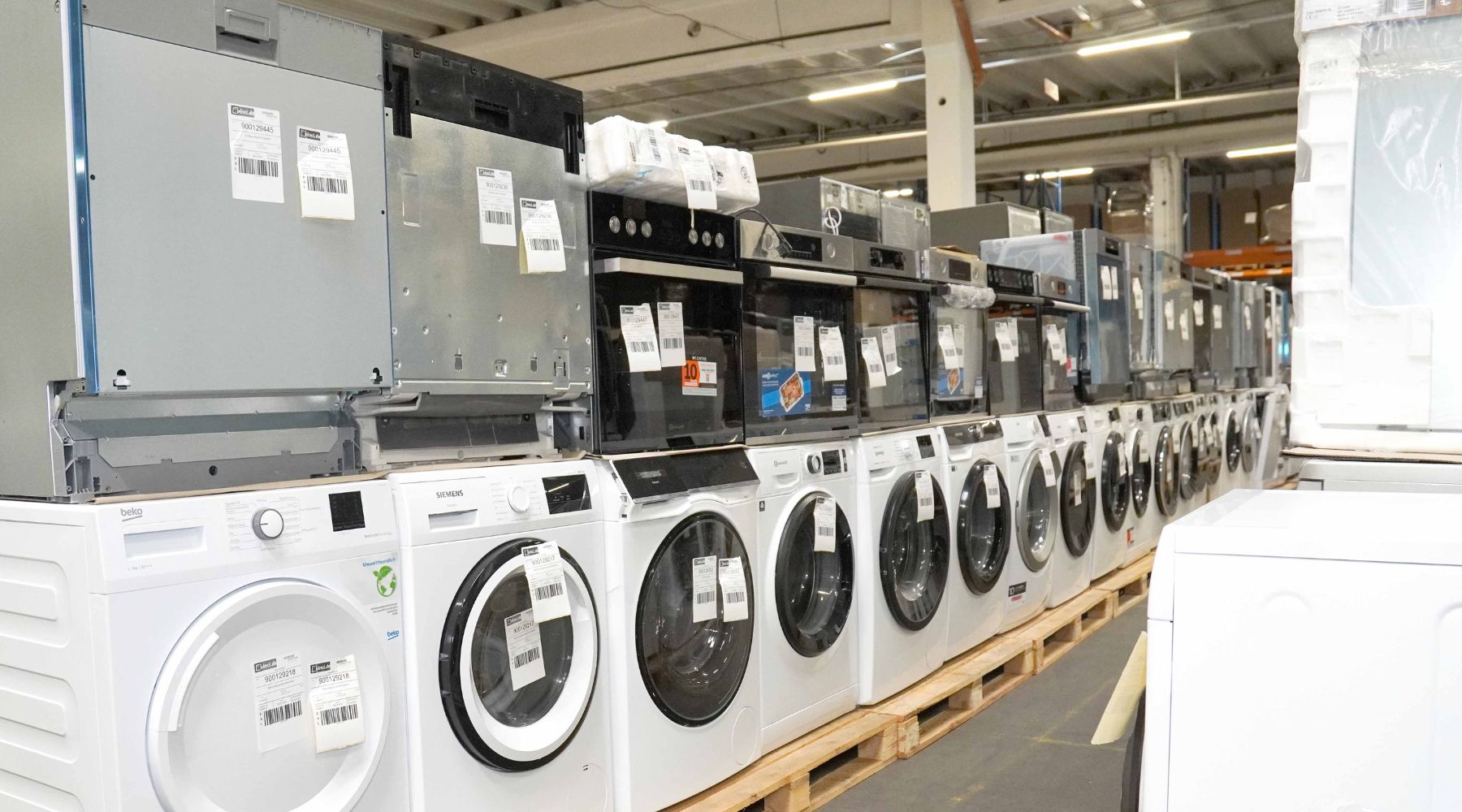 Reihe von Waschmaschinen und Einbaugeräten auf Paletten – typische Retouren Elektronik, die beim Kaufen und Wiederverkaufen von Palettenware sowohl Chancen als auch Herausforderungen für Händler bietet.
